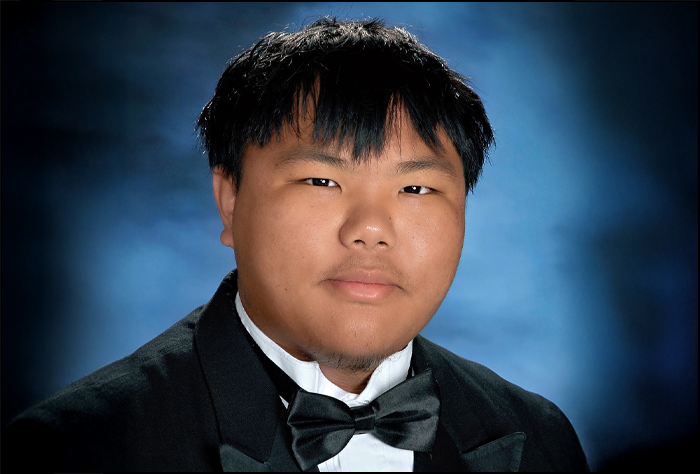 Young man in a black suite with black bow tie and blue background.