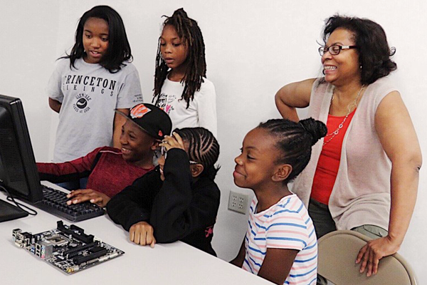 Smiling group of middle-school children with a smiling woman looking at a computer.