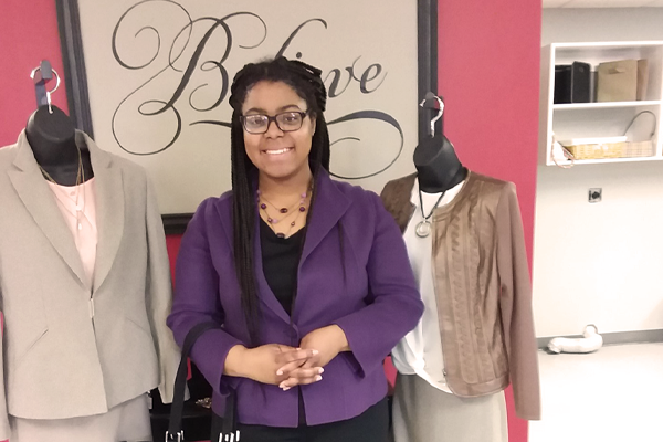 Photo of woman in purple suit coat in front of a Believe sign inside.