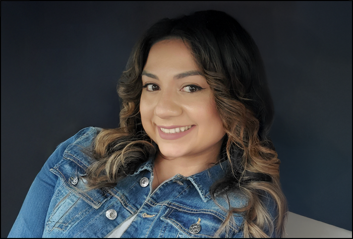 Smiling woman in a jean jacket leaning on a white couch.,