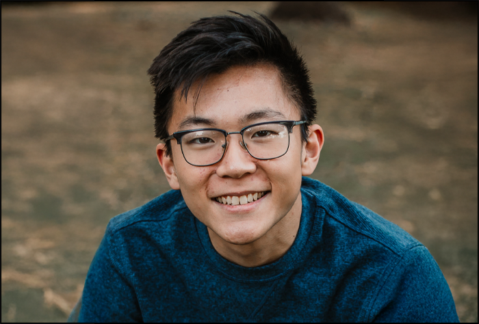 Smiling young man with glasses and a teal sweater outside.