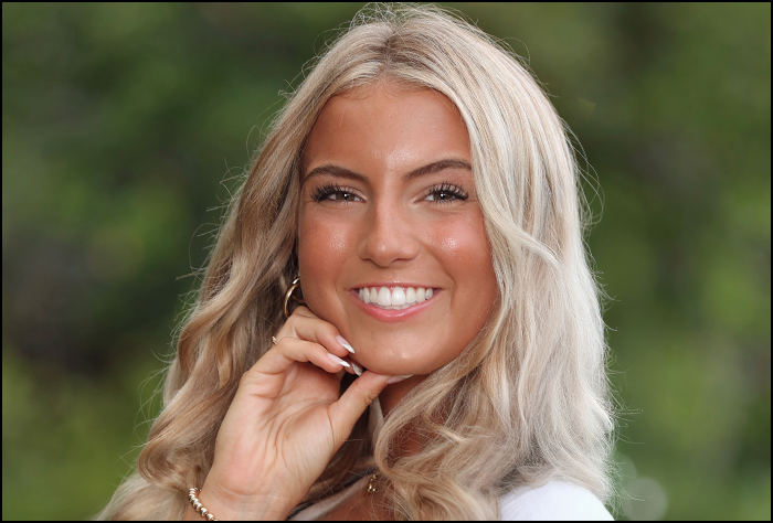 Smiling blonde woman with green background outside.