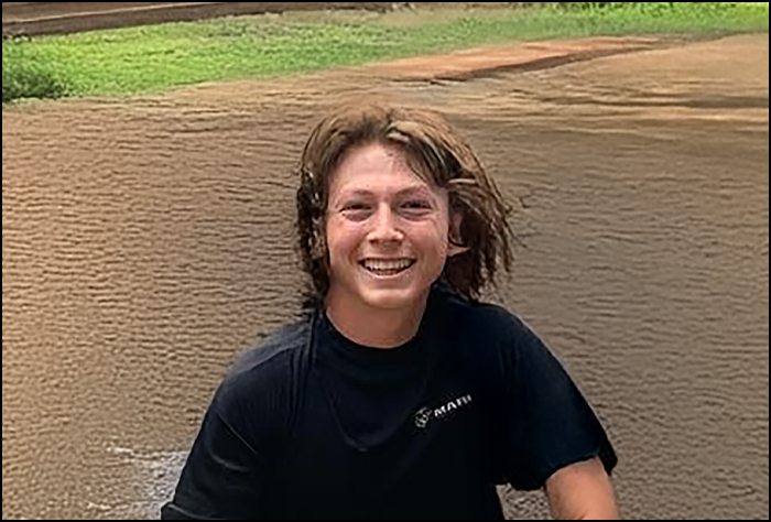 Smiling young man kneeling down in a black t-shirt outside.