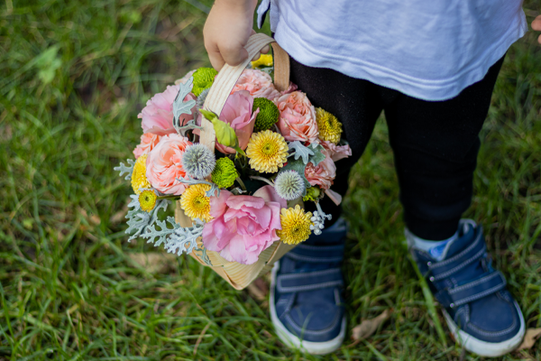 photo of A child holding a colorful flower basket outside on grass.