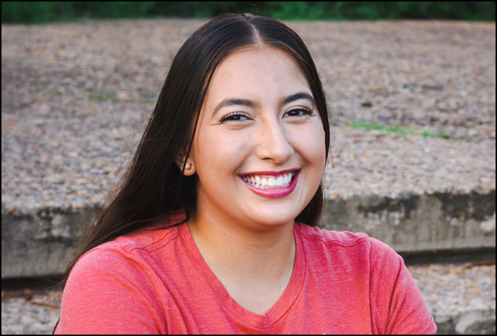 Smiling brunette woman in a coral color sweater outside.