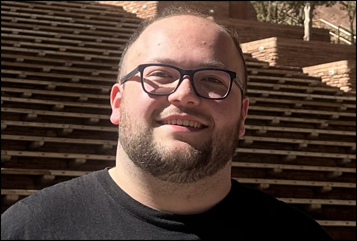 Smiling man with glasses and a beard outside in front of stairs.